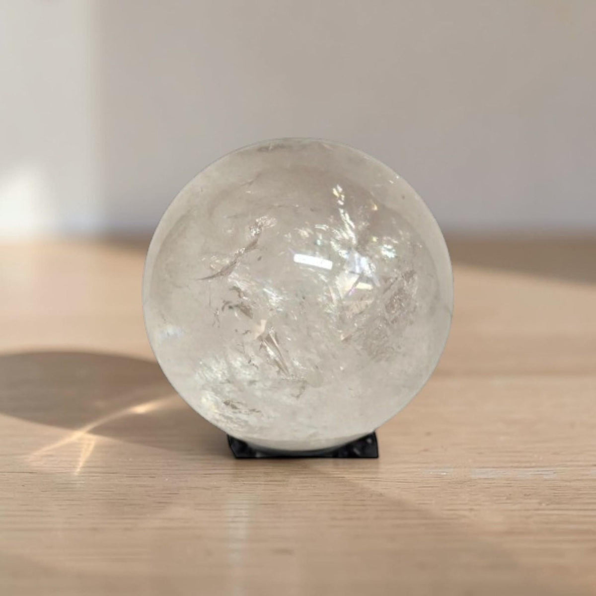 Polished clear quartz sphere gemstone on black display stand, detailed crystal inclusions