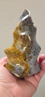 Freeform ocean jasper crystal flame held in hand, blue-gray with gold streaks and texture