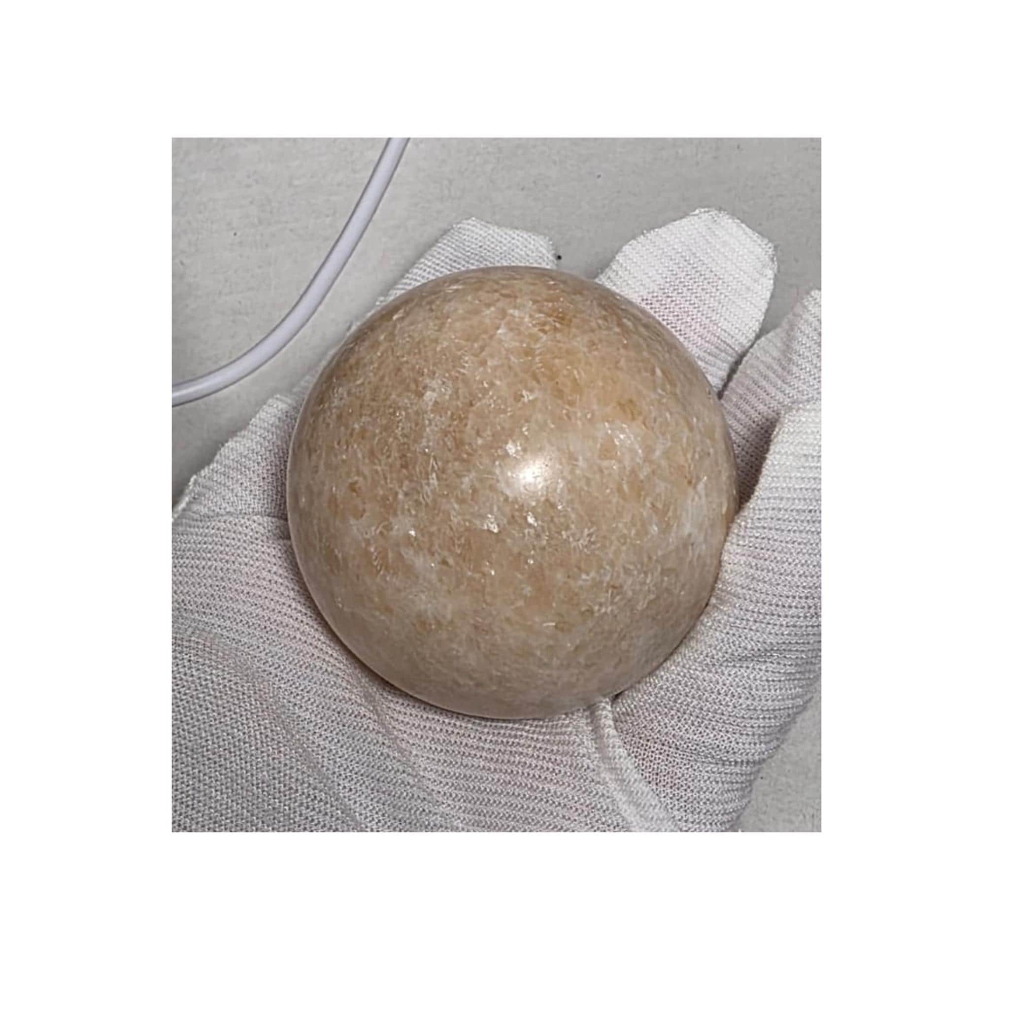 Honey calcite crystal sphere resting on light gray fabric, pale honey-gold finish