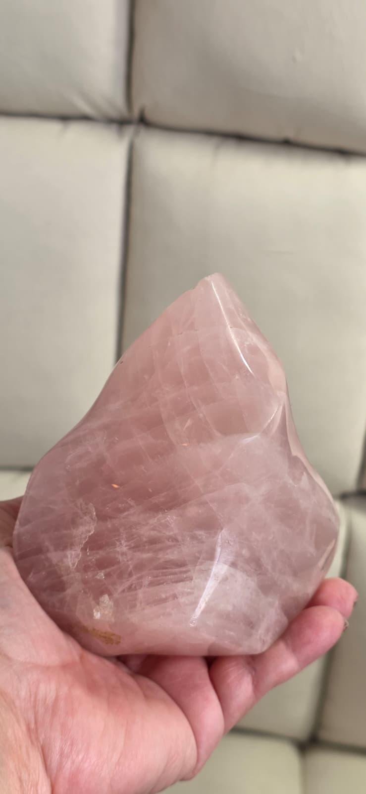 Rose quartz flame-shaped crystal held in hand, pink translucent with visible internal patterns