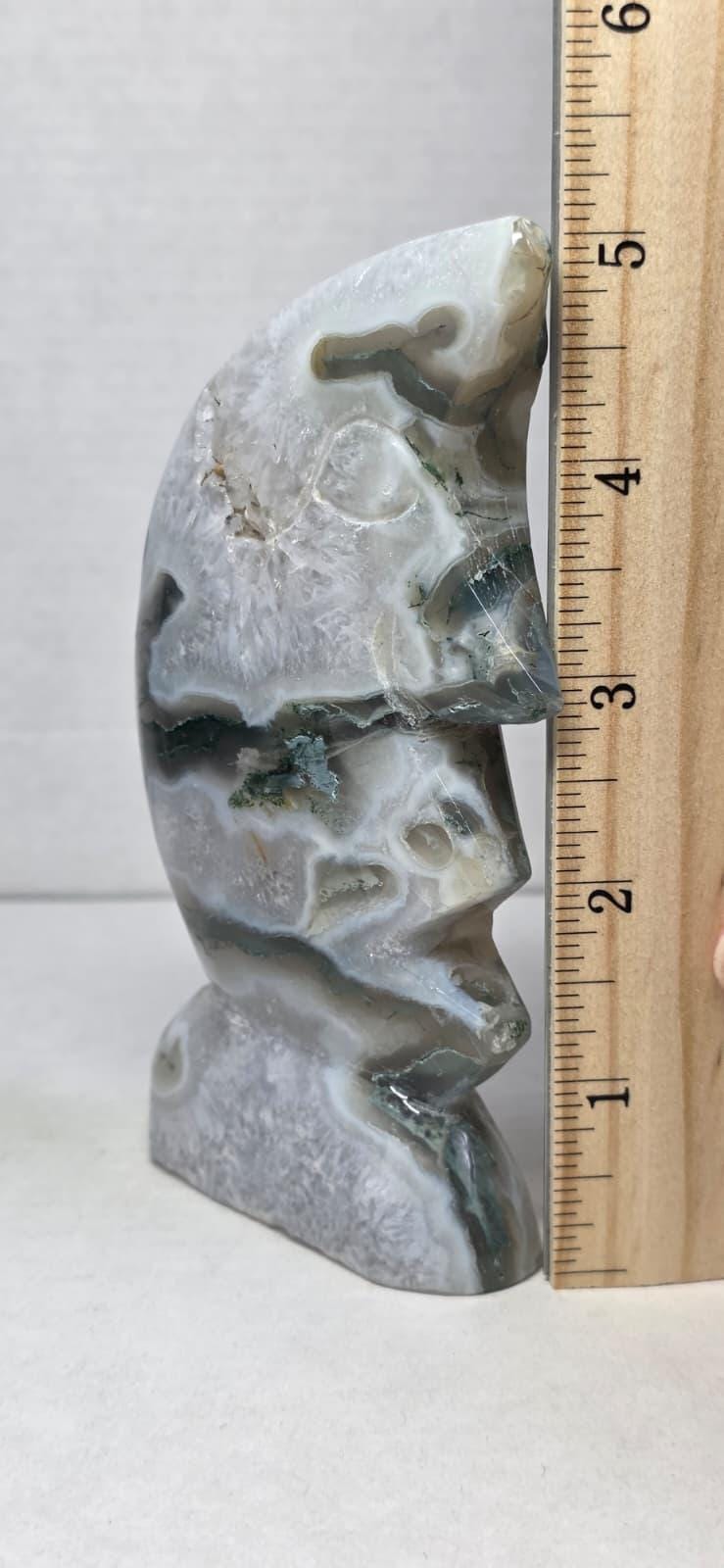 Moon face moss agate carving, light gray with green veining, shown next to wooden ruler