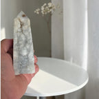 Agate drusy crystal tower, upright pointed top, white-gray with brown specks; held in hand.