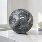 Moss agate geode sphere: dark gray-blue with green mossy patches and clear druzy quartz