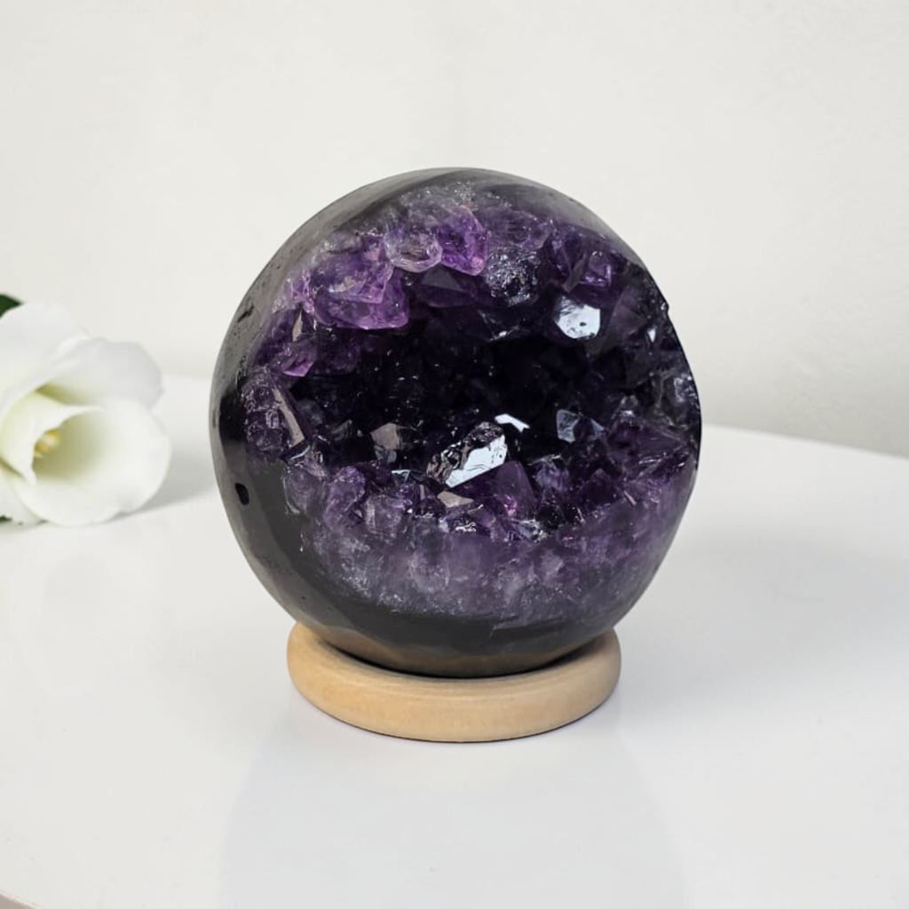 Amethyst geode crystal sphere on light wooden base, dark purple and black crystal interior