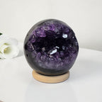 Amethyst geode crystal sphere on light wooden base, dark purple and black crystal interior