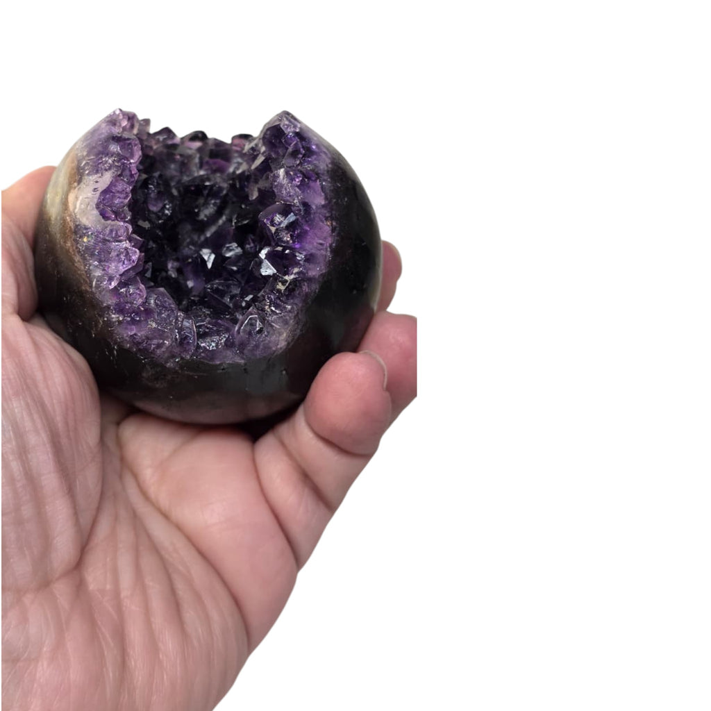 Amethyst geode sphere held in hand, faceted purple crystal cluster with dark backing
