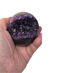 Amethyst geode sphere held in hand, purple crystal face with dark amethyst base