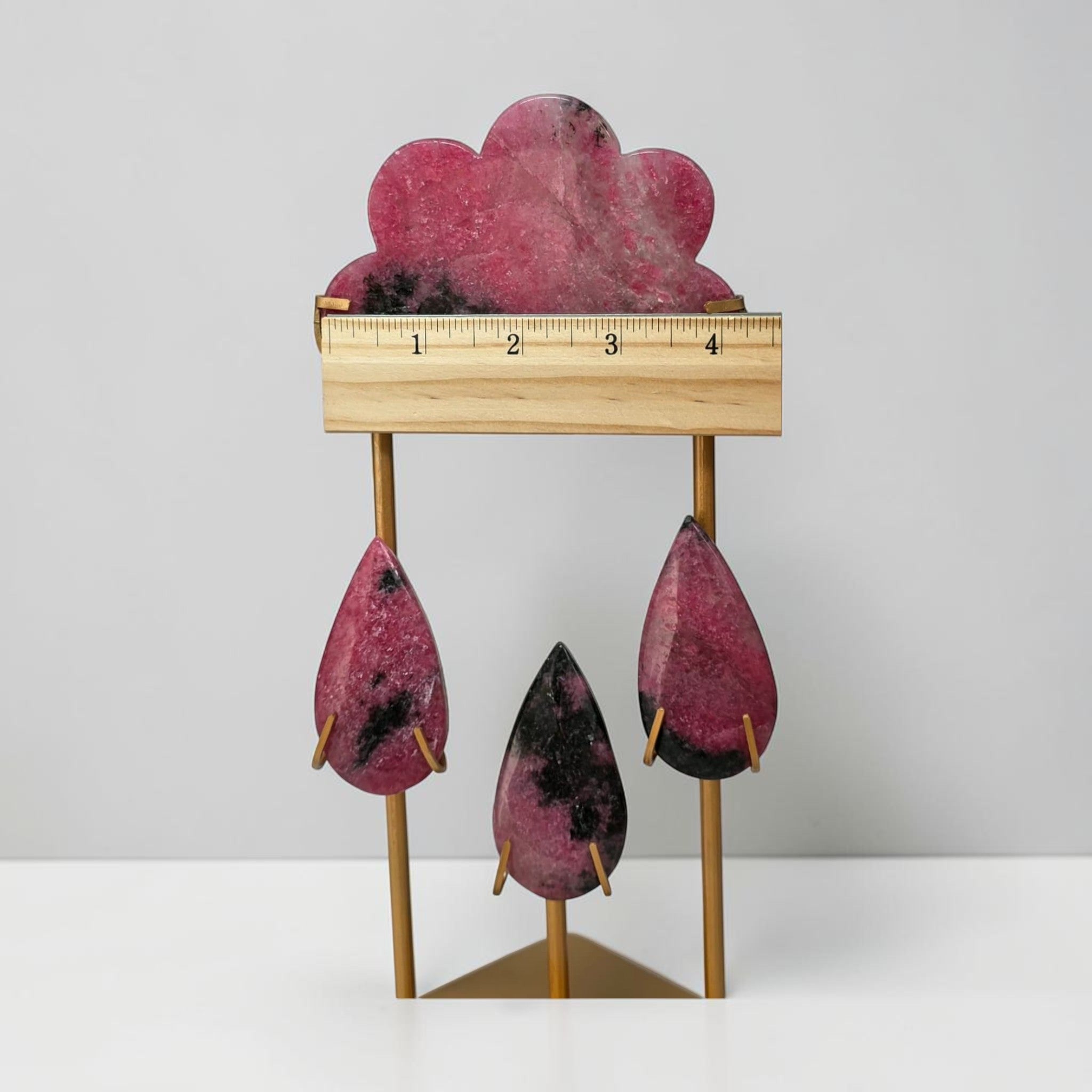 Rhodonite rain cloud crystal sculpture with ruler across top; pink cloud and hanging teardrops on stand