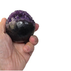 Amethyst geode sphere held in hand, purple crystal top over dark gray-black surface