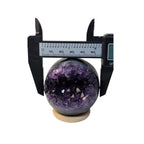 Amethyst geode crystal sphere with caliper gauge, dark purple and black crystal interior