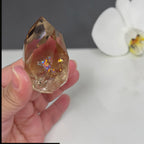 Smoky quartz crystal held in hand, faceted stone with iridescent rainbow highlights