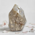 Agate flame crystal, clear beige with white druzy inclusions beside scattered flower petals
