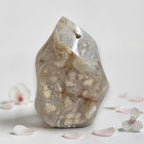 Agate flame crystal, clear beige with white druzy inclusions beside scattered flower petals