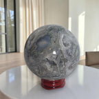 Grey agate geode sphere on red stand, blue-gray interior opening with cloudy texture