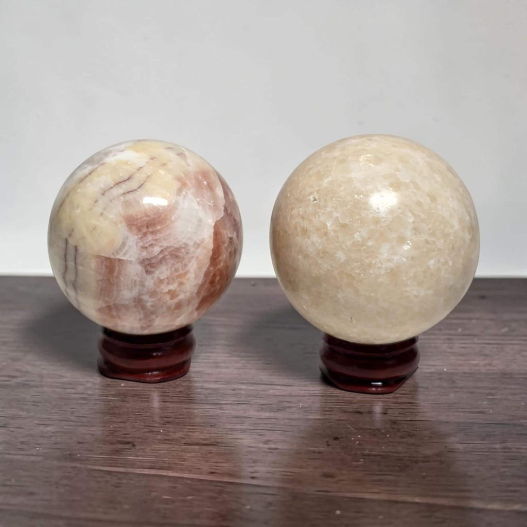 Two calcite spheres on dark wooden stands: pink veined left, pale cream right.