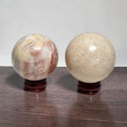 Two calcite spheres on dark wooden stands: pink veined left, pale cream right.