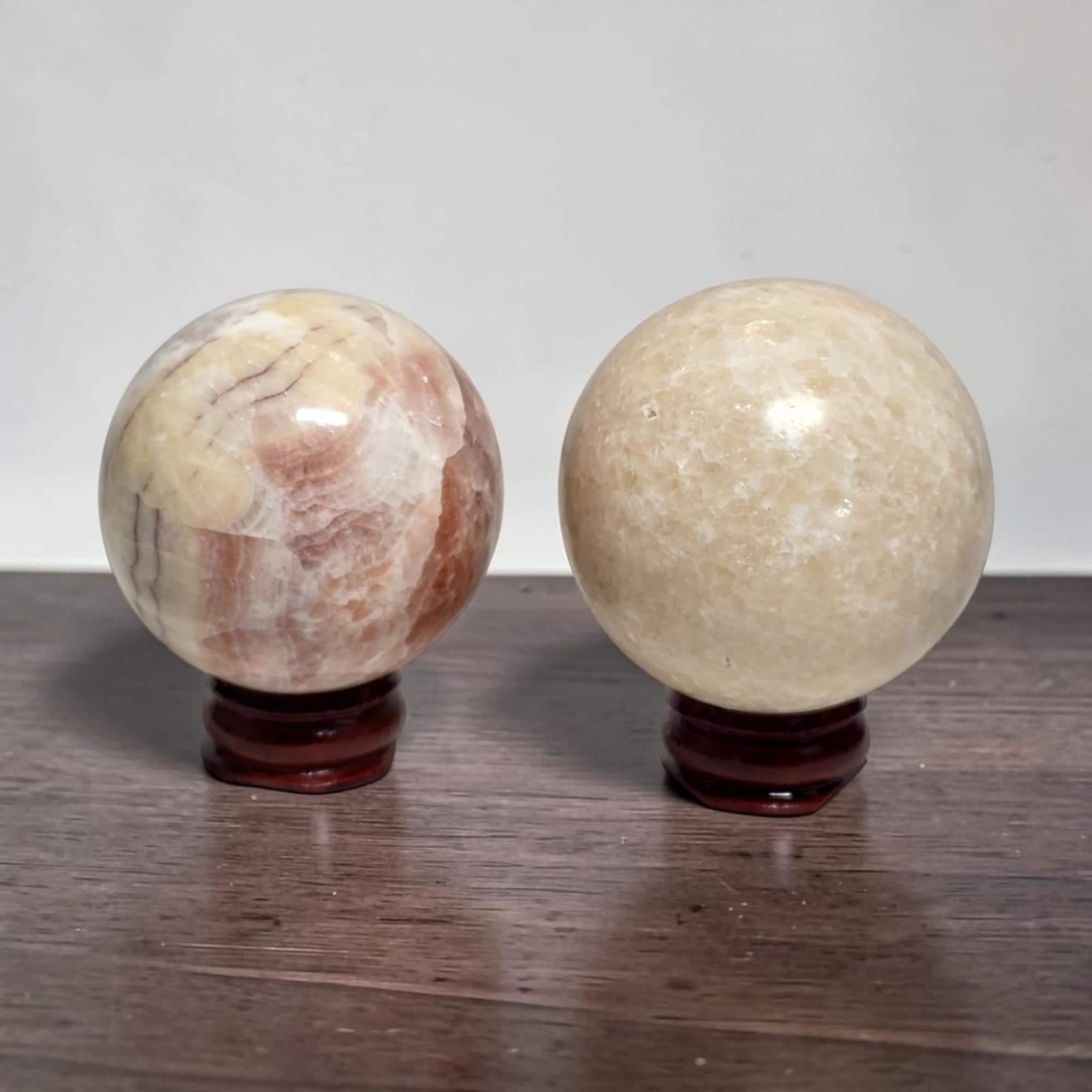 Two calcite spheres on dark wooden stands: pink veined left, pale cream right.