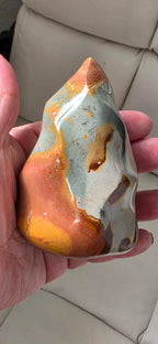Flame-shaped ocean jasper crystal held in hand; glossy blue-gray and rust-red