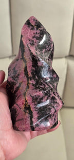 Polished rhodonite flame crystal carving with pink areas and dark streaks