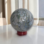 Grey agate geode sphere on red stand, detailed banding and druzy pockets