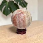Pink banded calcite sphere on dark wooden stand, polished with natural veining.