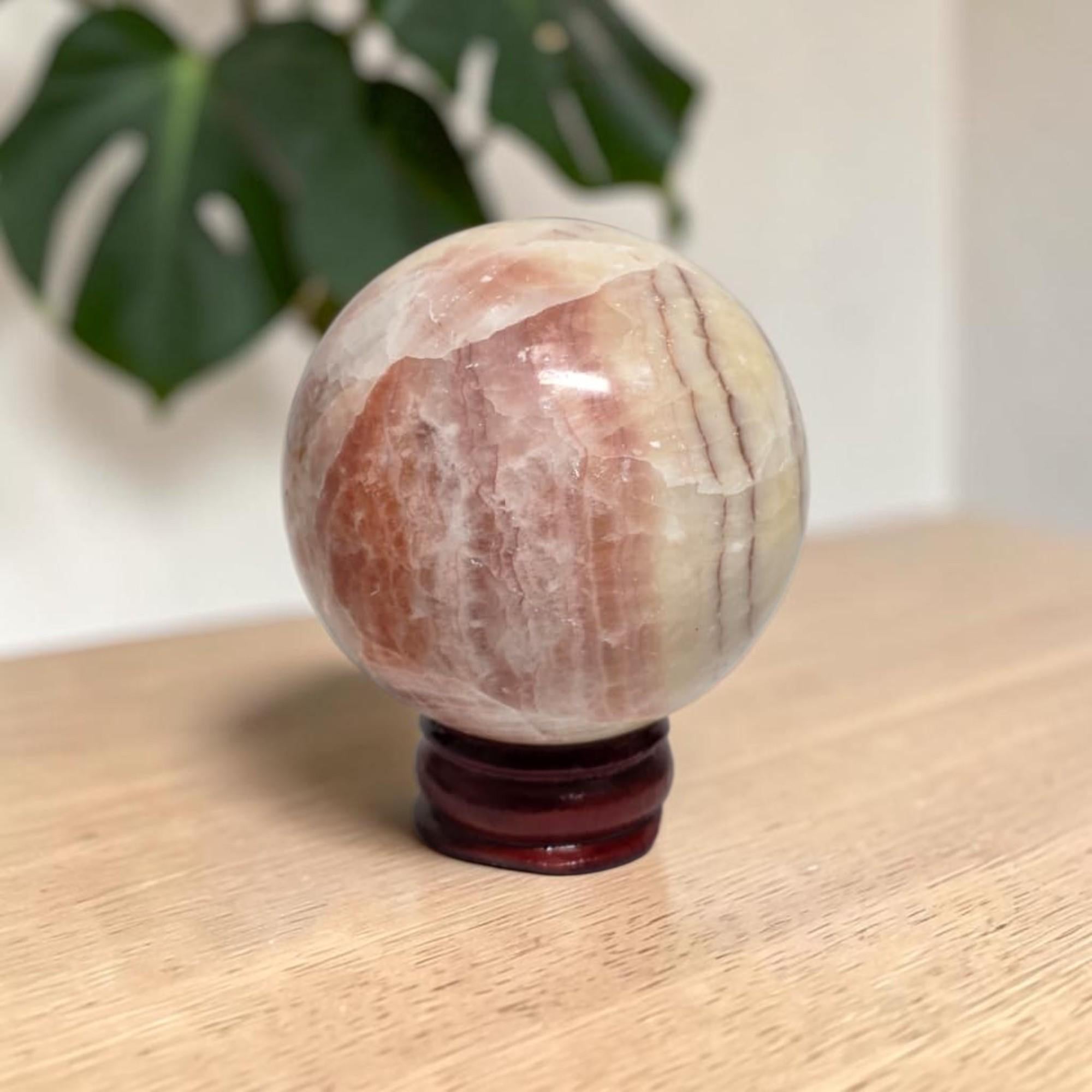 Pink banded calcite sphere on dark wooden stand, polished with natural veining.