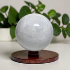 Calcite crystal ball sphere on dark wooden stand, translucent white-gray