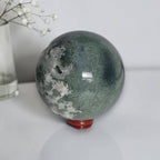 Green crystal sphere with speckled texture and white druzy inclusions on red base
