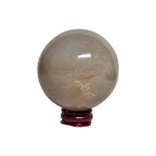 Honey calcite crystal sphere on dark red stand, translucent beige with subtle golden flecks