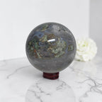 Moss agate geode sphere: dark gray-blue with green and tan mineral streaks and white druzy