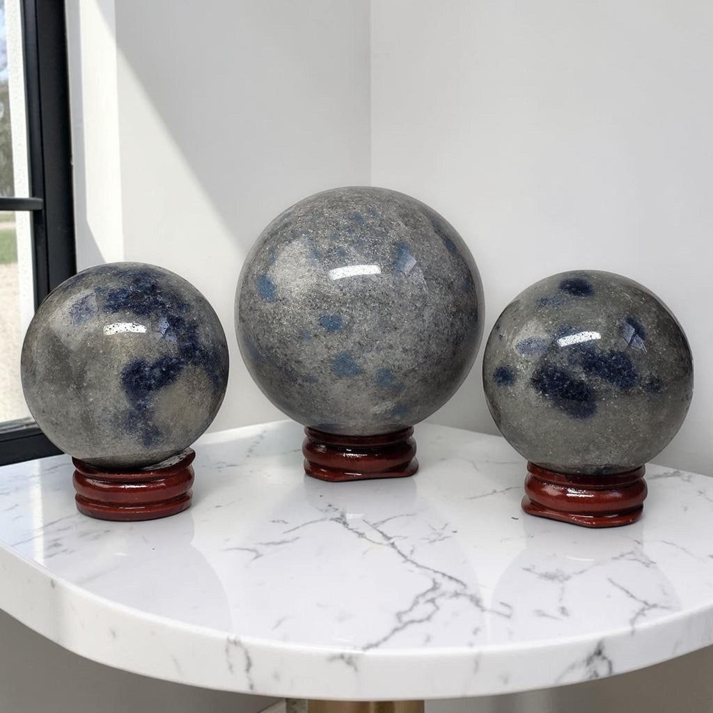 Set of three polished granite crystal spheres with blue mottling on red stands