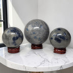 Set of three polished granite crystal spheres with blue mottling on red stands