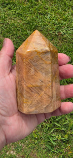 Obelisk point tower stone held in hand, polished brown-gold with pointed top