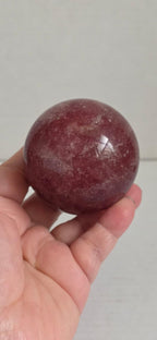 Deep red crystal sphere held in hands, glossy polished surface