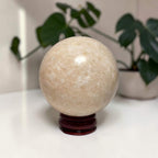 Honey calcite sphere on dark wooden stand, pale honey-gold with sparkly texture
