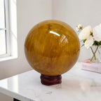 Amber golden crystal sphere on dark wooden stand with reflective surface