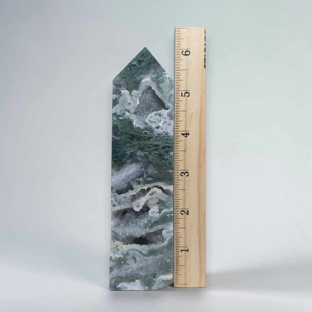 Green moss agate drusy obelisk tower crystal beside a wooden measuring ruler
