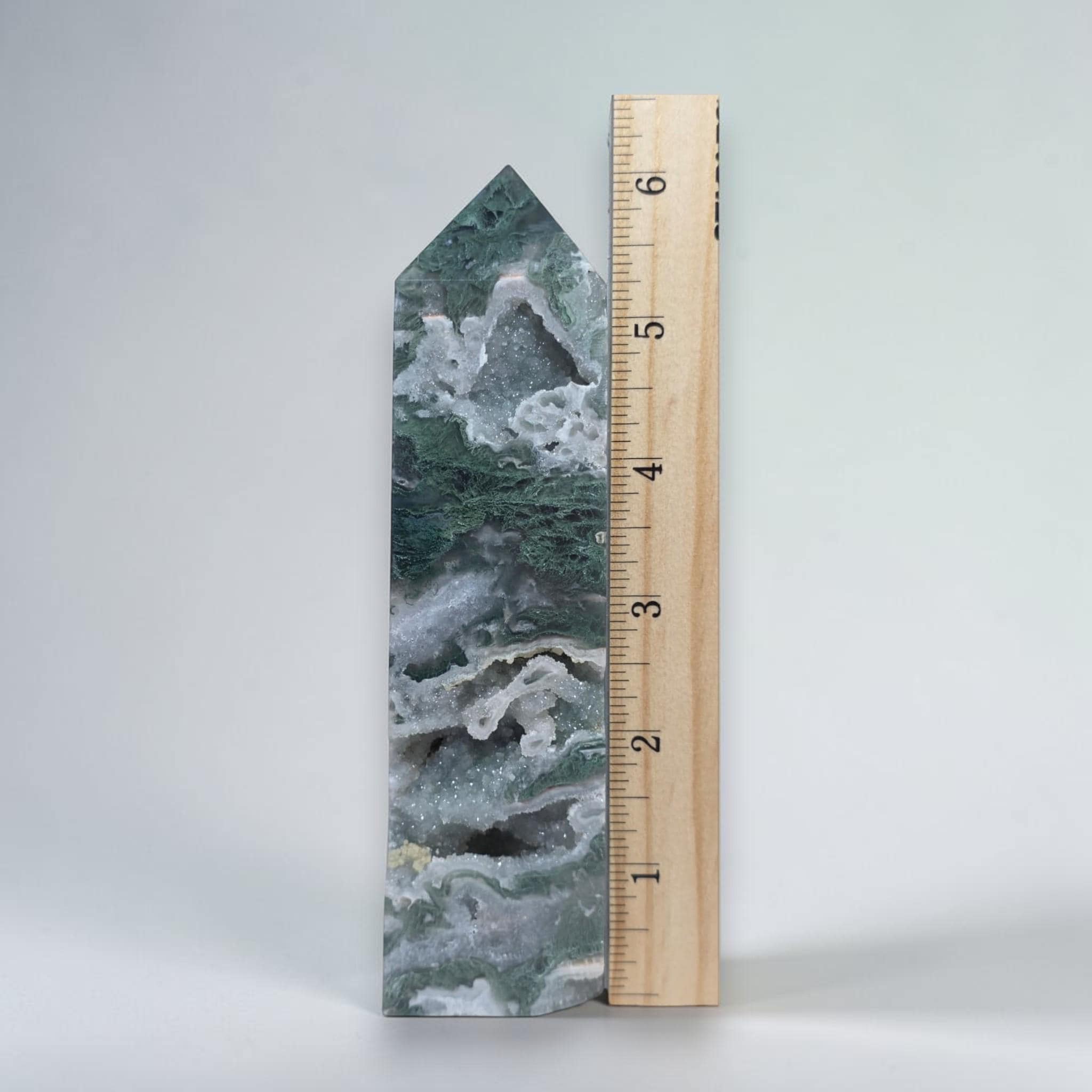 Green moss agate drusy obelisk tower crystal beside a wooden measuring ruler