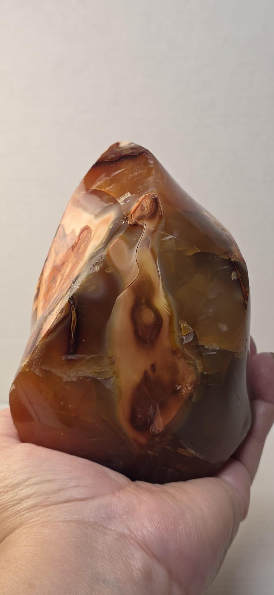 Polished orange agate flame crystal held in hand, glossy facets and dark swirls