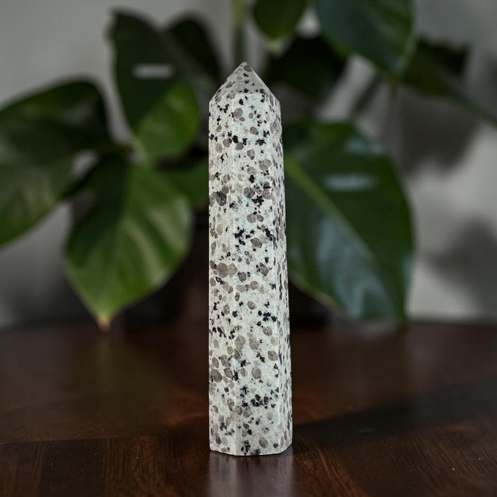 Polished speckled jasper obelisk, pointed crown, white with scattered dark mineral flecks.