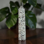 Polished speckled jasper obelisk, pointed crown, white with scattered dark mineral flecks.