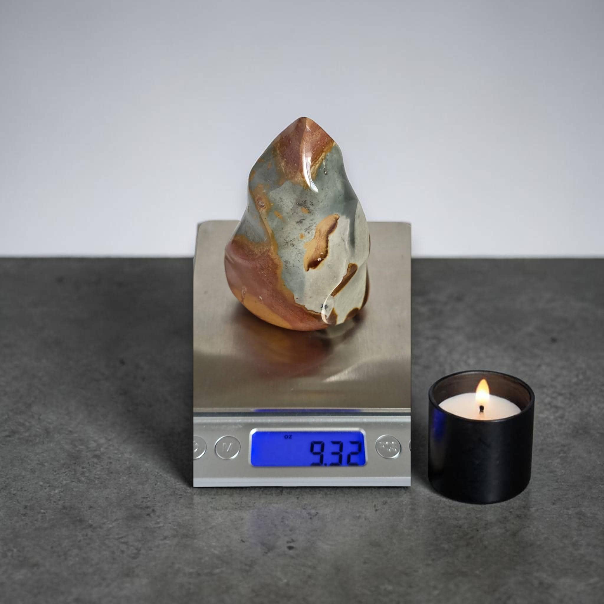 Flame-shaped ocean jasper crystal on scale with lit candle; blue-gray and red