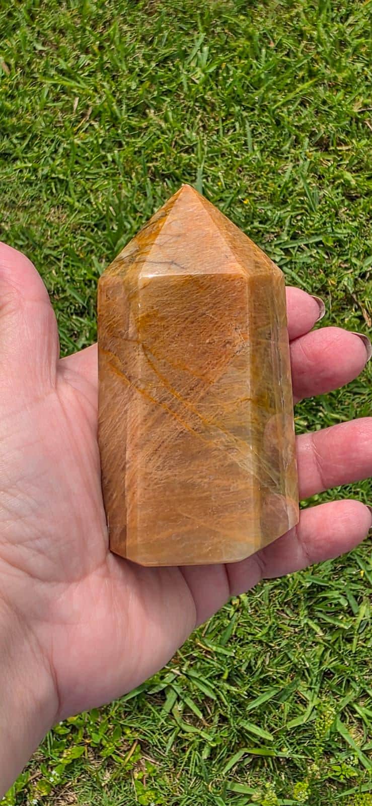 Obelisk point tower stone in hand, polished amber-brown with faceted surface