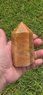 Obelisk point tower stone in hand, polished amber-brown with faceted surface