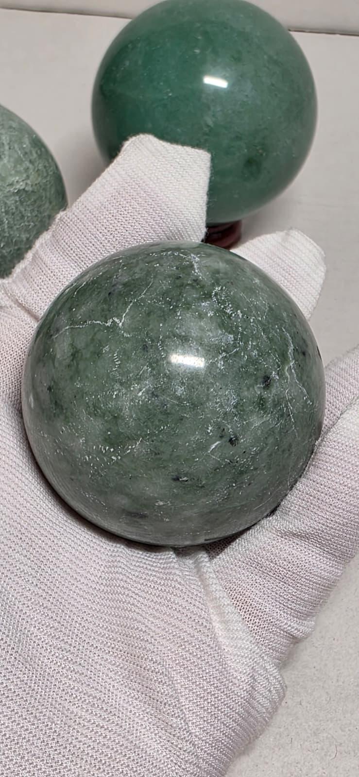 Green and gray-green crystal spheres on white gloves, maroon bases