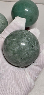 Green and gray-green crystal spheres on white gloves, maroon bases