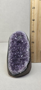 Amethyst druzy freeform crystal stone with purple sparkling surface beside a wooden ruler