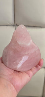 Rose quartz flame-shaped crystal held in hand, pink translucent with bright reflective surface