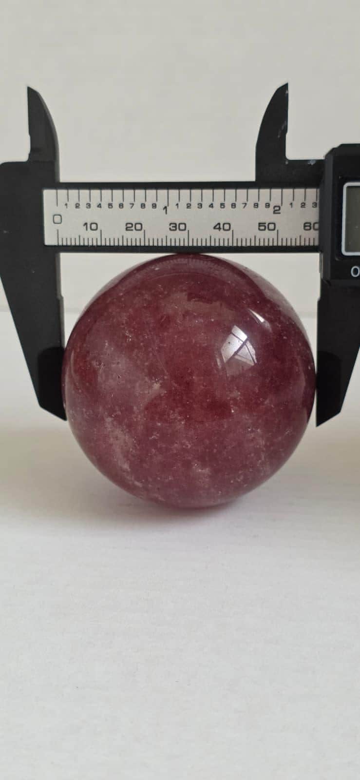 Deep red crystal sphere measured with a black caliper
