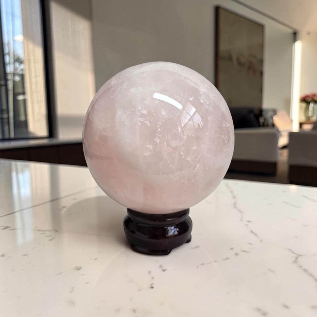 Rose quartz sphere on dark stand, polished pale pink crystal ball